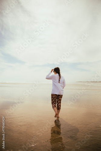 Barefoot girl with ponytail and white shirt walking along the beach photo