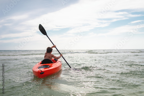 Boy paddling an ornage kayak in the vast blue ocean photo
