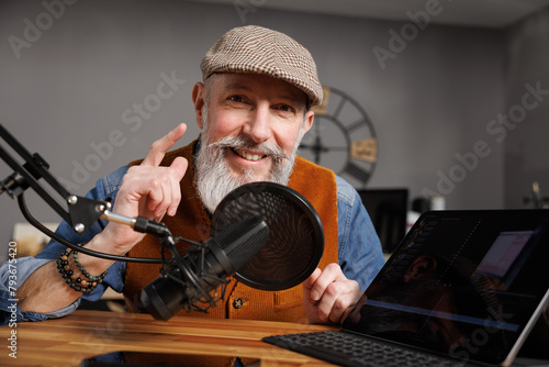 Studio podcast avec un micro et un ordinateur tablette et un homme souriant au look stylé et vintage avec une barbe hipster © Chlorophylle