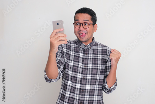 A man showing funny excited expression when looking to mobile phone that he hold