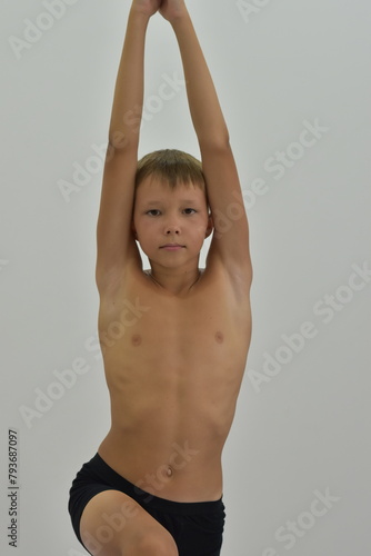 A fair-haired boy stands in a yoga pose with his arms raised.
