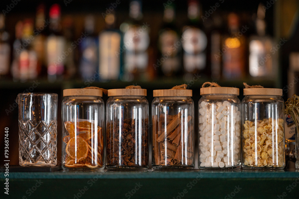 Glass jars with dried herbs, spices, berries and citrus fruits, prepared by hand, create a unique mixological atmosphere. Glass jars with dried herbs, spices, berries and citrus fruits, prepared by hand, create a unique mixological atmosphere.