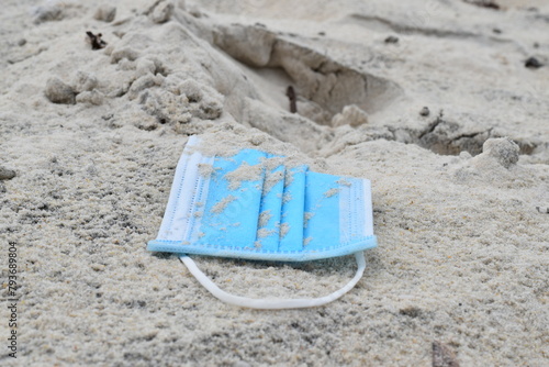 A blue medical mask against the virus is buried in white sand.