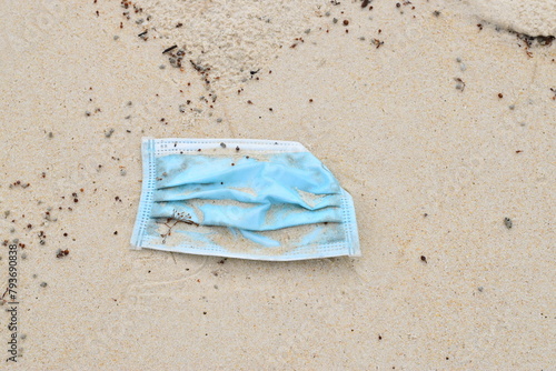 A blue medical mask lies on the white sand.