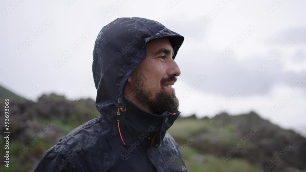 Young smiling Caucasian man in dark blue mackintosh in natural landscape looking with satisfaction at place. Happy handsome male feeling freedom and peace in Nature enjoying on holiday while raining Young smiling Caucasian man in dark blue mackintosh in natural landscape looking with satisfaction at place. Happy handsome male feeling freedom and peace in Nature enjoying on holiday while raining