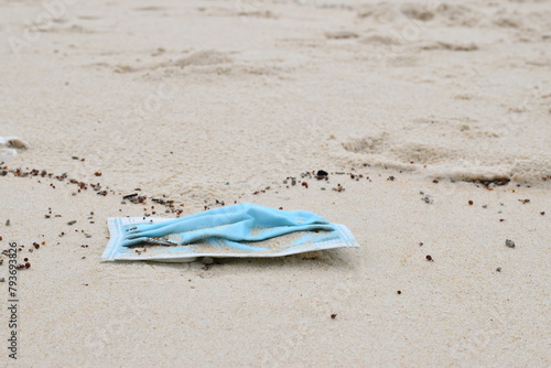 A dirty blue medical mask lies on the white sand.