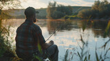 A man fisherman sits on the river bank with a fishing rod