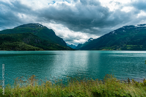 Mountain lake in Norway. Turquoise water of lake of glacial origin. Delightful amazing view of the landscape of Scandinavia northern Europe mountains. Beautiful glacier is visible in the distance.