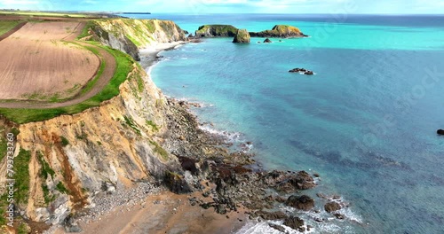 Drone flying over headland with sandy cliffs eroding into the sea and rockfalls on the beach with crystal clear water and deep blue colours Copper Coast in Waterford Ireland on a spring afternoon photo