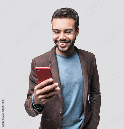 Portrait of handsome cheerful smiling young man using smartphone isolated on gray background. Laughing joyful men with mobile phone studio shot