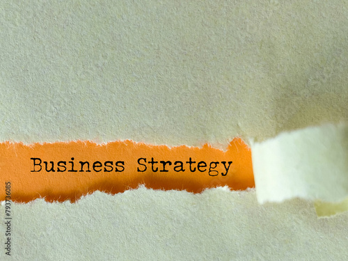 Business strategy text behind torn paper background. Stock photo.