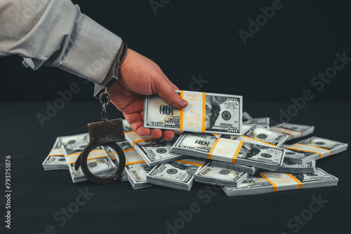 Financial fraud. An official in handcuffs wanted to steal a wad of dollars from a pile of money on a black background. A hand in a handcuff reaches for money on a black background.