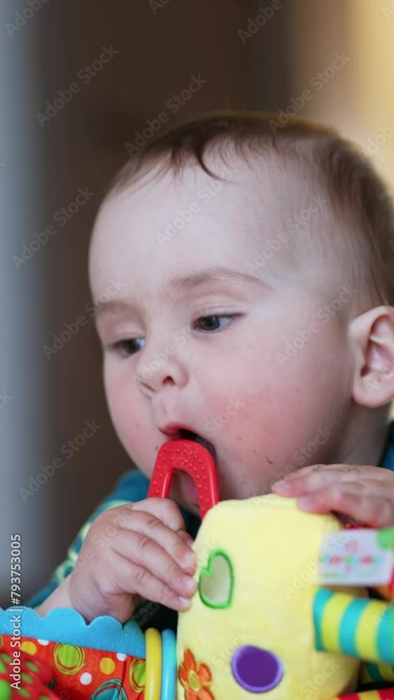 Beautiful little baby lies on floor playing with a toy. Child pulls a chewing rubber ring from a toy to his mouth. Close up. Blurred backdrop. Vertical video Beautiful little baby lies on floor playing with a toy. Child pulls a chewing rubber ring from a toy to his mouth. Close up. Blurred backdrop. Vertical video