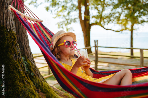 The child drinks a cocktail through a straw and relaxing in a hammock in nature.