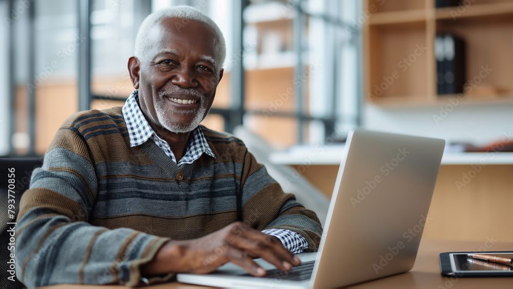 An elderly African American man with a warm, friendly smile is sitting at a table and working on a laptop. An elderly African American man with a warm, friendly smile is sitting at a table and working on a laptop.
