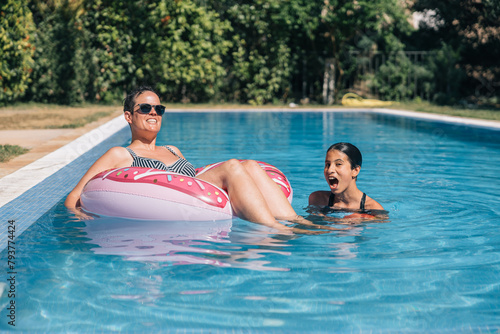 A mother and daughter are in a pool, the woman sitting on a pink float and the girl splashing around © Amparo Garcia