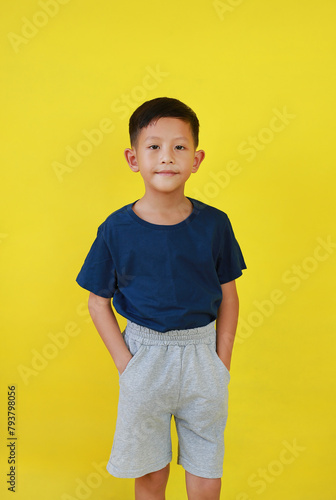 Smiling Asian little boy child put hand in his pocket of pants and looking straight over yellow studio background.