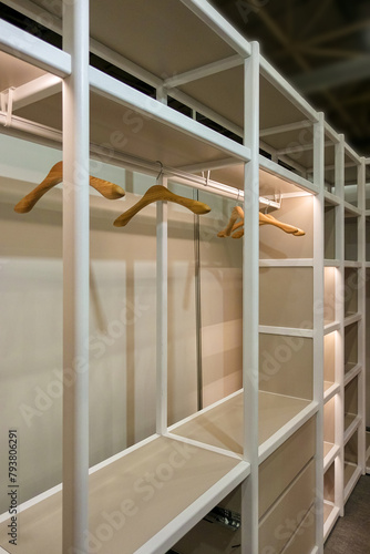 Spacious empty dressing room in white with shelves and wooden hangers. The overall look of the closet is neat and organized.