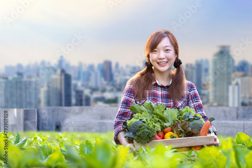 Asian woman gardener is harvesting organics vegetable while working at rooftop urban farming futuristic city sustainable gardening on the limited space to reduce carbon footprint and food security