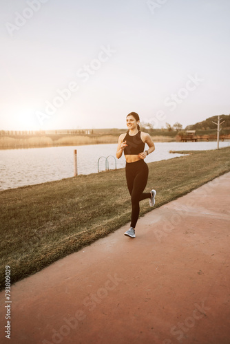 A young woman in sportswear runs along the embankment at sunset. The concept of a healthy lifestyle