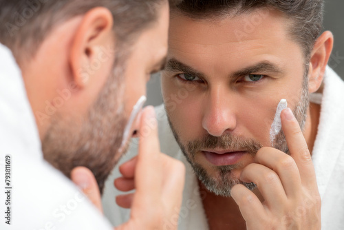 Man applying face cream. Beauty routine. Man with perfect skin. Anti-aging and wrinkle cream. Concept of male beauty. Close up face of man applying cream to skin. Skincare and cosmetics concept.