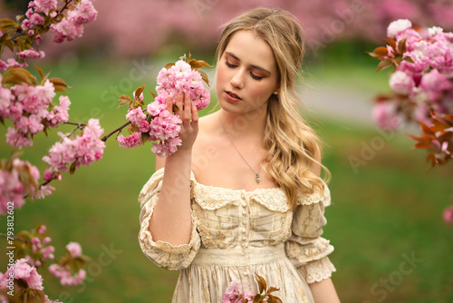 Pretty young blonde girl  in vintage lace dress  standing in spring park near pink blossom flowers. Tenderness romantic  model posing 