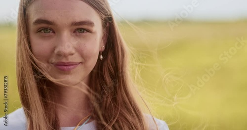 Close up portrait of young girl turning her head, looking at camera. Non urban scene, windy day, yellow field, candid child smilng, natural beauty, ukrainian teenager. High quality 4k footage photo