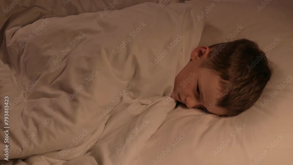 small child boy tosses restlessly in sleep on a pillow under a blanket at night. Sleeping preschooler kid son on a bed in the bedroom in the evening small child boy tosses restlessly in sleep on a pillow under a blanket at night. Sleeping preschooler kid son on a bed in the bedroom in the evening