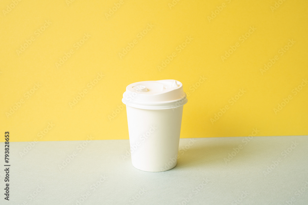 Disposable paper coffee cup on gray table. yellow wall background