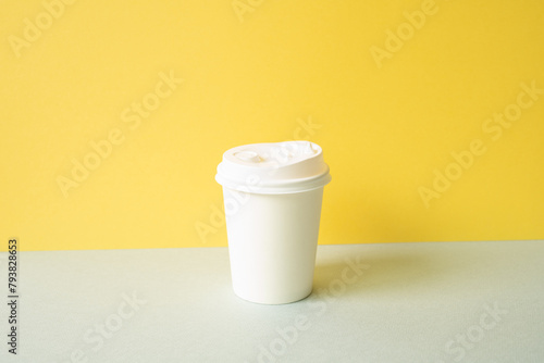 Obraz na płótnie Disposable paper coffee cup on gray table. yellow wall background w salonie