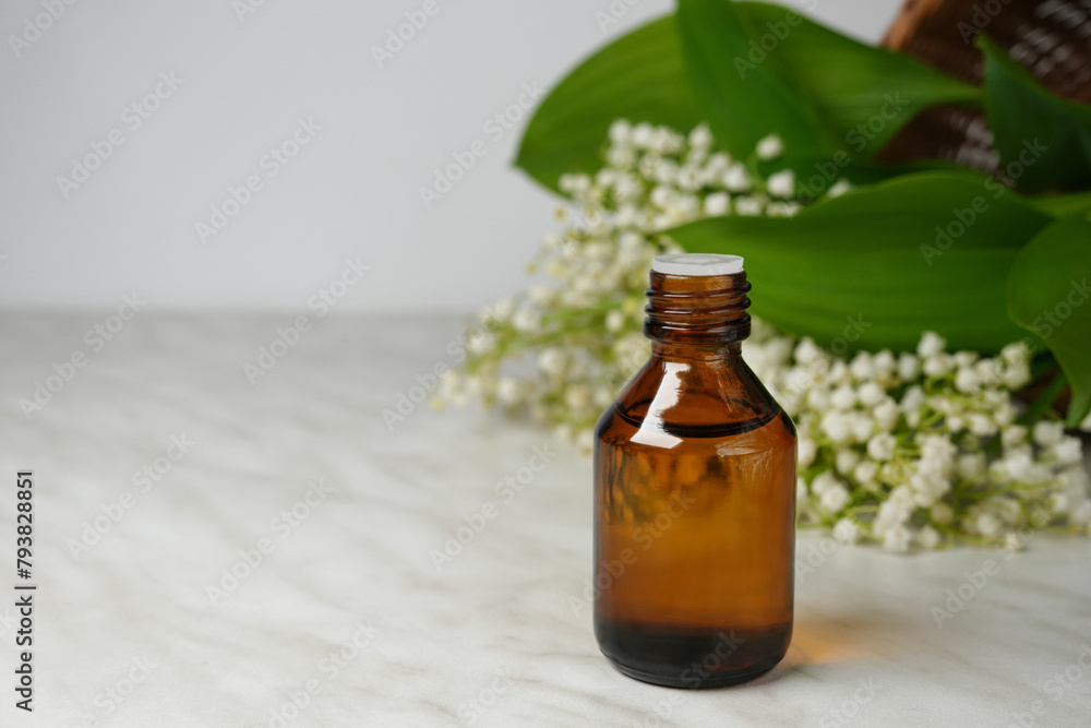 Lily of the valley essential oil in a small bottle. Essence of flowers on a white marble table. Side view.Space for text.