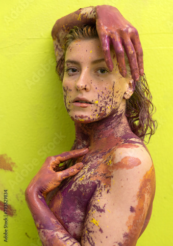 Portrait of a young artistically abstract woman in pink and yellow painted against light green wall background