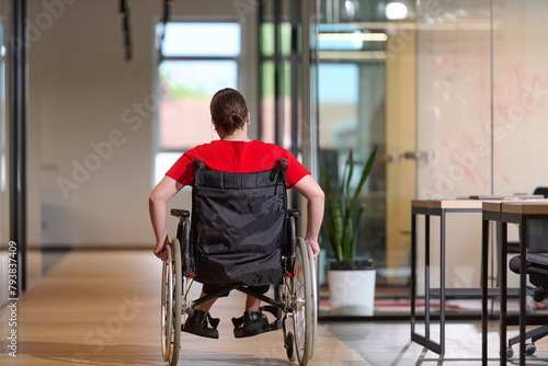 A modern young businesswoman in a wheelchair is surrounded by an inclusive workspace with glass-walled offices, embodying determination and innovation in the business world