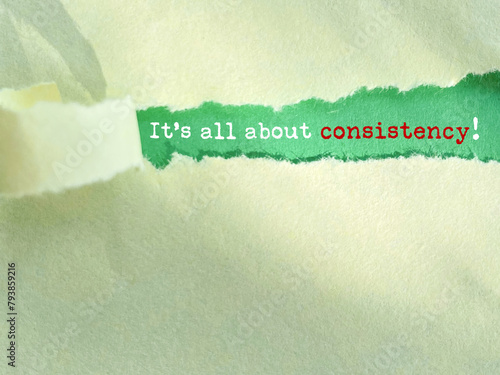 Inspirational success quote - It's all about consistency text behind torn paper background. Stock photo.