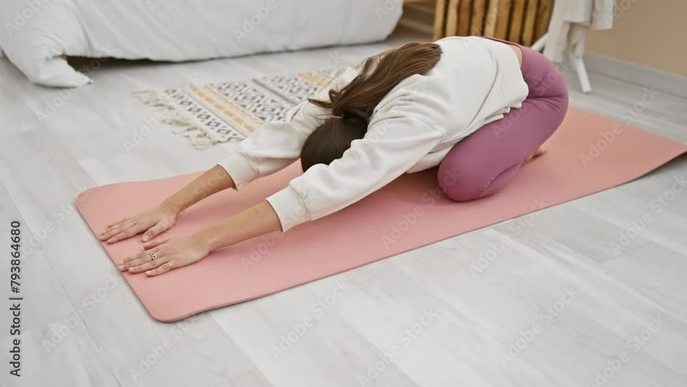 A young woman in activewear practices yoga on a pink mat in a bright, modern bedroom. A young woman in activewear practices yoga on a pink mat in a bright, modern bedroom.