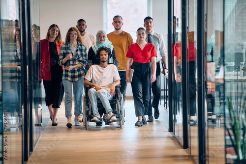A diverse group of young business people congregates within a modern startup's glass-enclosed office, featuring inclusivity with a person in a wheelchair, an African American young man, and a hijab © .shock