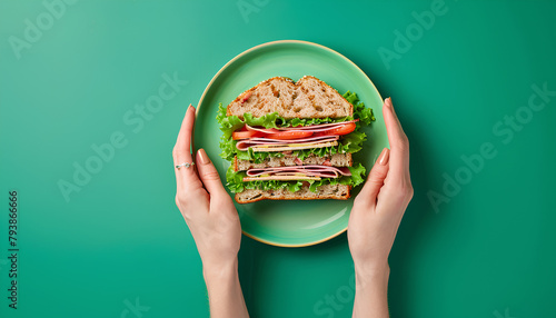Female hand holding plate with delicious ham sandwich on green background photo