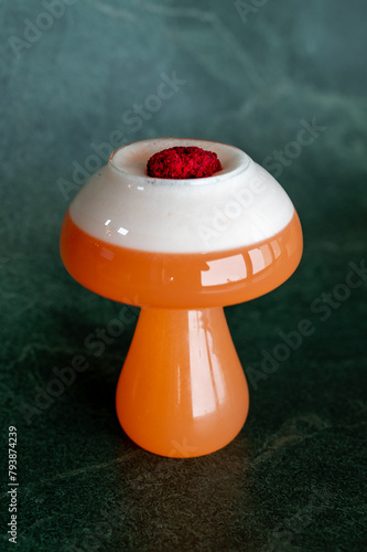 Innovative cocktail in a curvy orange glass, crowned with frothy foam and a bold red garnish. A feast for the senses, blending art and taste. (ID: 793874239)