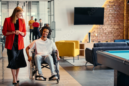A diverse group of young professionals, including businesswomen and an African-American entrepreneur in a wheelchair, engage in collaborative discussion on various business projects in a modern