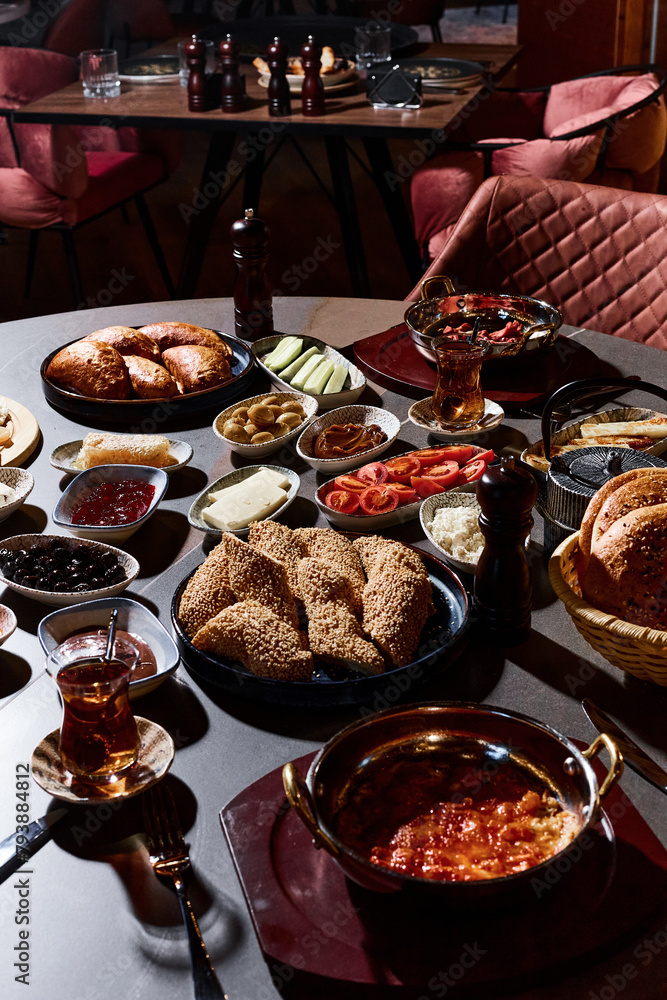 A sumptuous Turkish lunch, the menu of which presents a symphony of flavors. The menu includes bread, cheeses, sliced fresh fruits, pickled vegetables, snacks, hummus. Turkish tea in bowls.