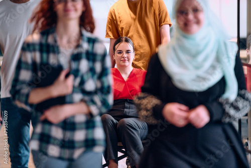 A diverse group of young business people walking a corridor in the glass-enclosed office of a modern startup, including a person in a wheelchair and a woman wearing a hijab © .shock