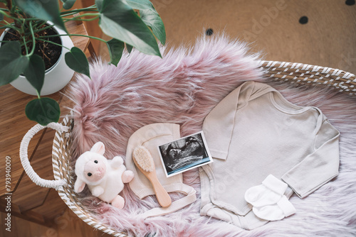 Baby changing basket with ultrasound image, baby bodysuit, soft and wooden toys. Still life of child products. Newborn background. Minimalist style photography of baby shower, pregnancy announcement.