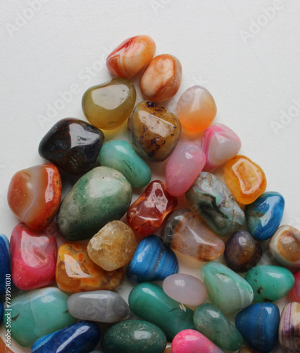 Colored rough gemstones in a triangle heap on white surface detailed top view 
