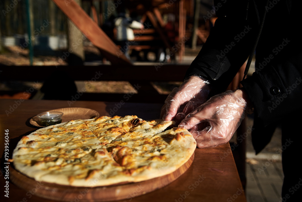 A delicious round pizza on a wooden tray lying on table.Hands picking up a slice of traditional italian four cheeses pizza in outside restaurant.Simple snack.Unhealthy food.Nutrition rules. Close-up
