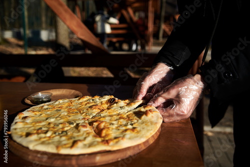 A delicious round pizza on a wooden tray lying on table.Hands picking up a slice of traditional italian four cheeses pizza in outside restaurant.Simple snack.Unhealthy food.Nutrition rules. Close-up