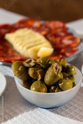 A dish of vibrant green olives is set against a backdrop of traditional Alentejo cheese and cured sausage. The scene captures the essence of Portuguese cuisine in a cozy restaurant setting.