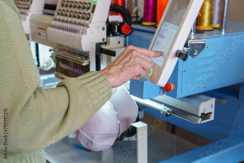Man's hand pointing onthe screen of embroidery machines next to colorful threads  and cap. Setting up a modern embroidery machine.