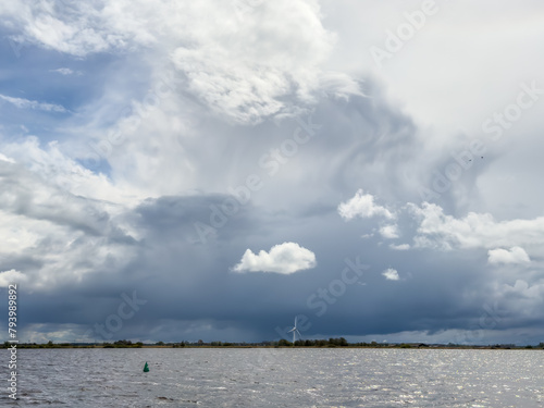 Single windmill on the edge of a lake rotating in storm wind against ominous, dark stom sky, regenerating renewable, sustainable energy and electricity photo