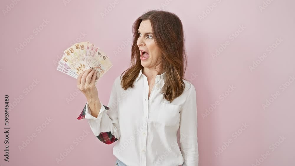 Shocked middle age woman clutching turkish lira, mouth open in amazed disbelief, fear etched on her face over isolated pink background. Shocked middle age woman clutching turkish lira, mouth open in amazed disbelief, fear etched on her face over isolated pink background.