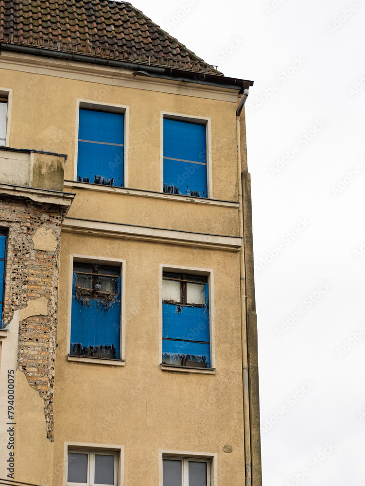 Broken windows of an abandoned residential building. Pigeons sitting in holes of the facade. The exterior of the property is weathered and run down due to poverty in the region.
